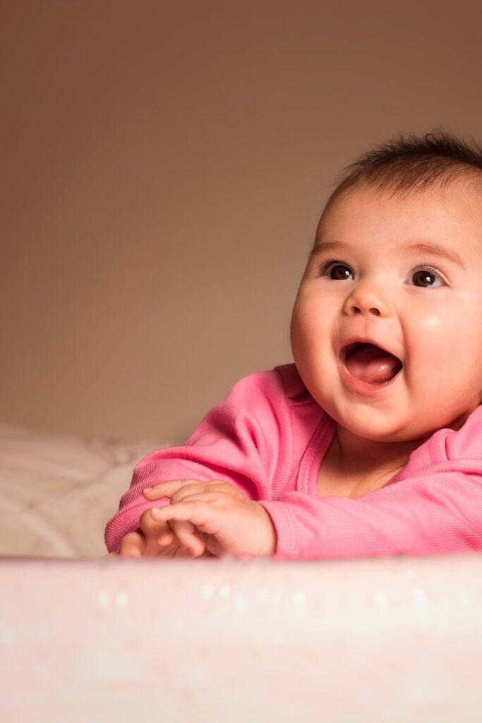 Charming portrait of a smiling baby girl in pink indoors, exuding happiness and innocence.